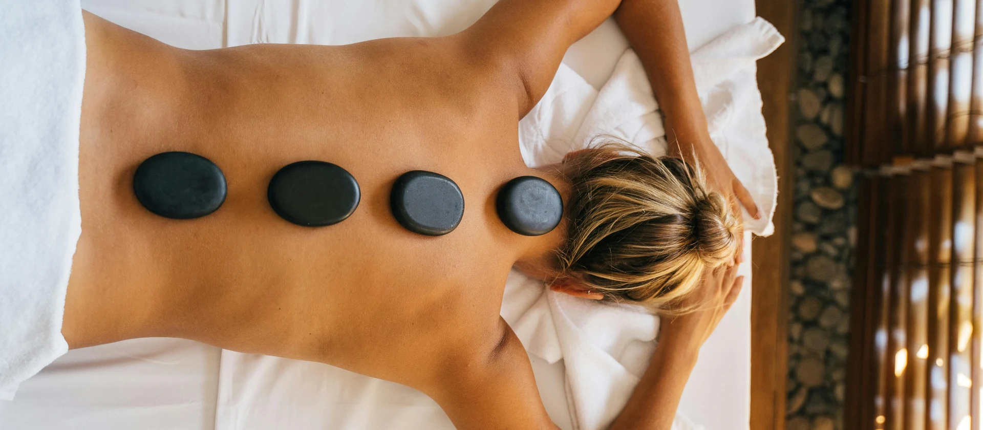 Hot stones placed across the back during a massage session, used to represent treatment prices and timings.